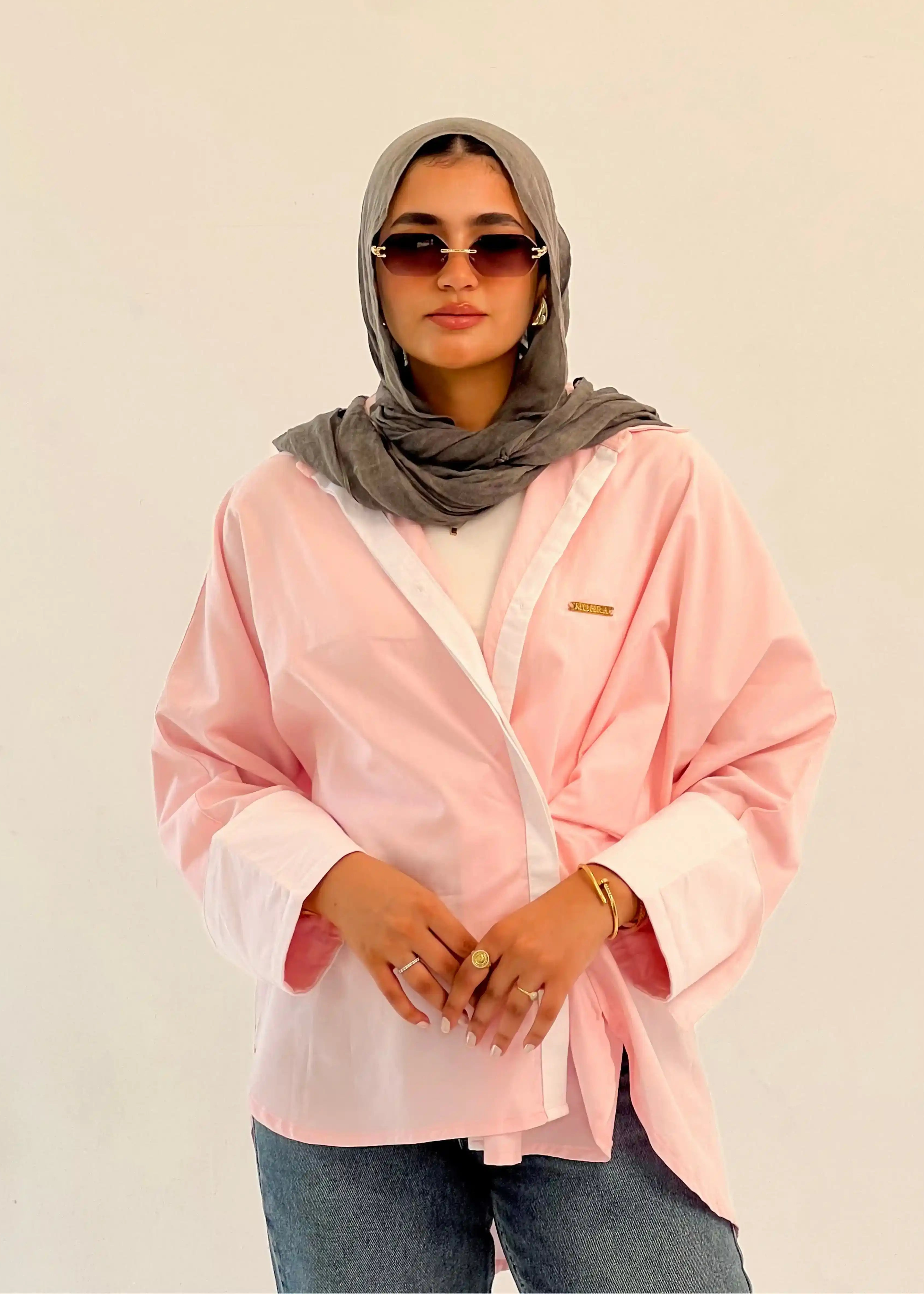 Person wearing a pink shirt, gray hijab, and sunglasses against a beige background